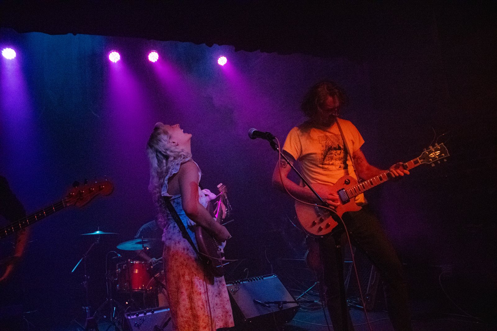 duo onstage under purple lights, vocalist in floral dress and guitarist in yellow tee
