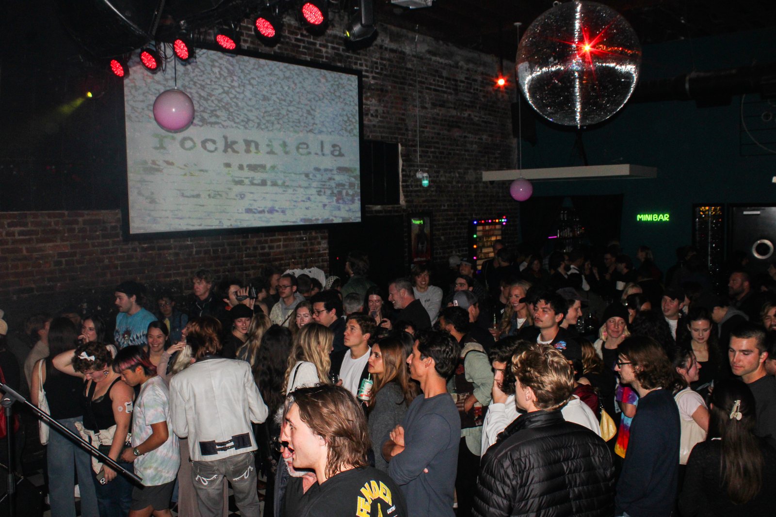packed crowd under a disco ball with the rocknite.la projection on the back wall