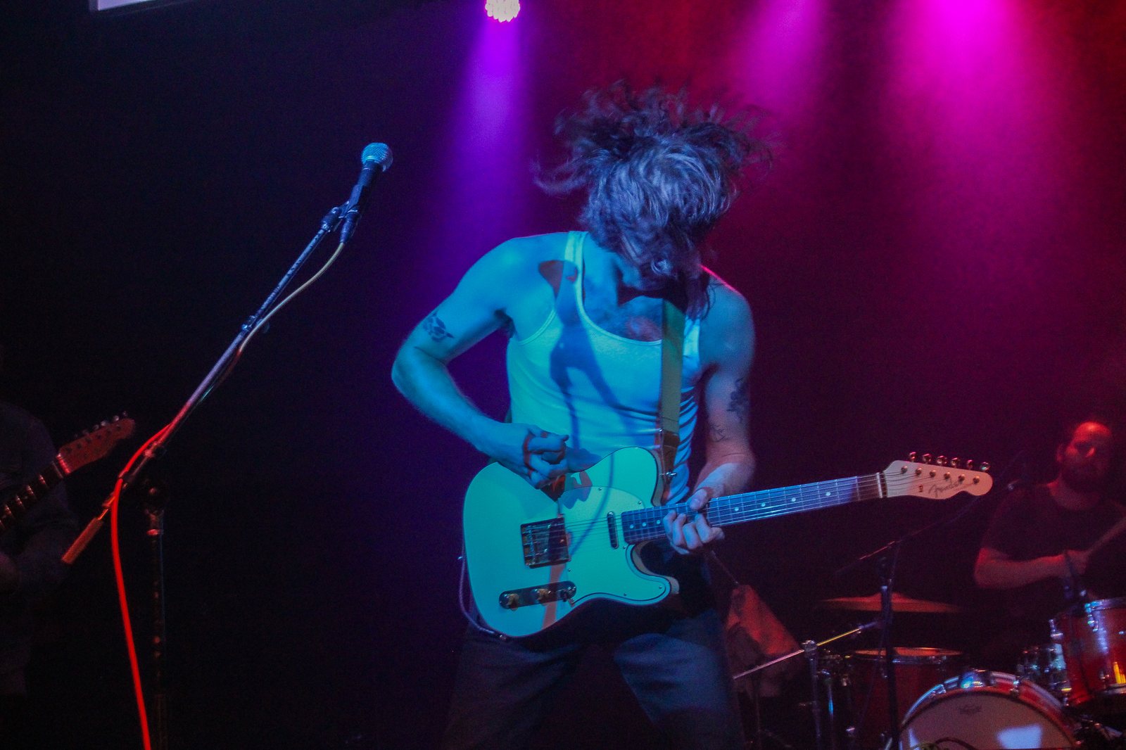 performer mid-song with hair flying, playing a mint-green telecaster under magenta lights