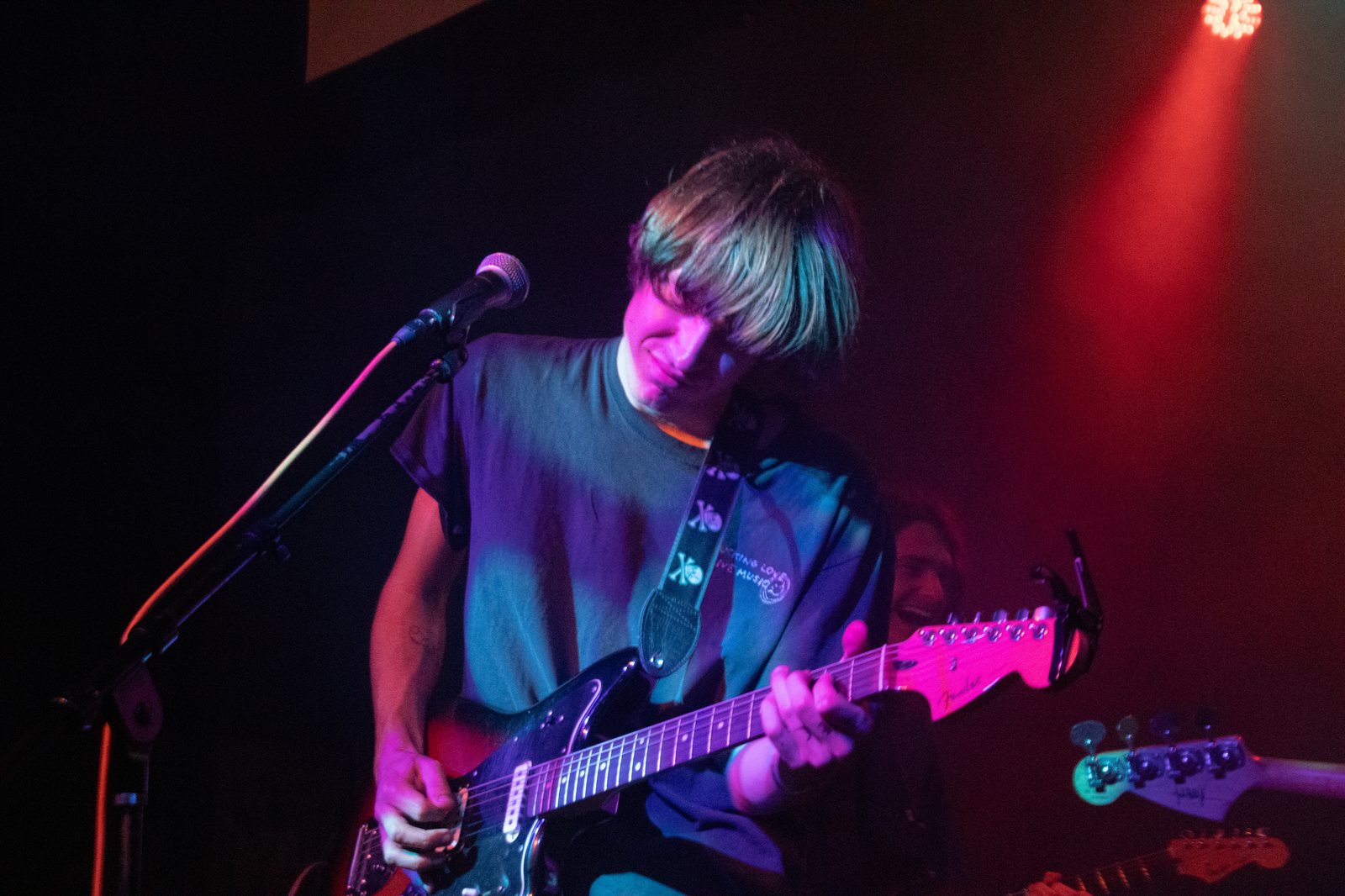 solo guitarist leaning into the mic in a moody pink and blue spotlight